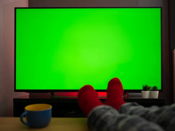 feet up on the table in front of green screen tv televison chroma key at home