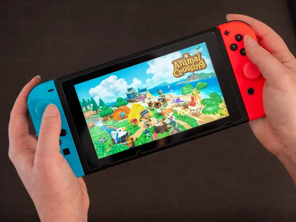 İngiltere, Mart 2020: Nintendo Switch el ele oyun konsolu kadın oyuncu elleri karanlık arkaplan üzerinde hayvan geçişi oynuyordu