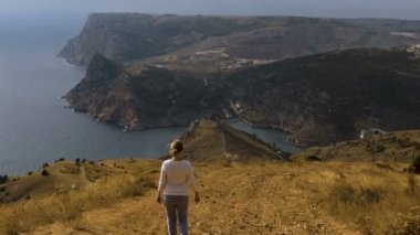 Kız yol boyunca dağın tepesinden denize iner. Odağı kızdan kıyıya değişir. Deniz manzarası, üstten görünüm.