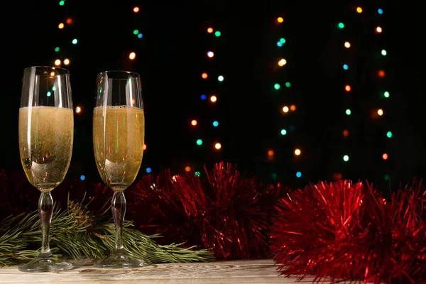 Christmas and New Year dinner of a couple with two glasses of champagne. The concept of the celebration. Pearls, tinsel and spruce branch on a black background with blurred lights.