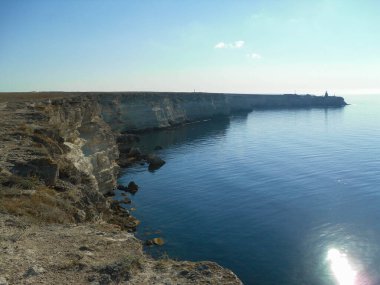 Yüksek sarp kıyı kayalıkları ve sonunda bir bina var. Güneşli bir gün, büyük mavi bir gökyüzü ve denize bir yolculuk.