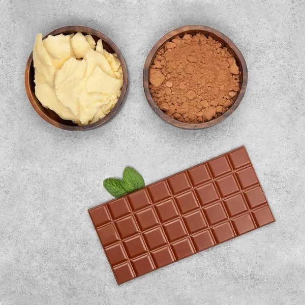 Bar of milk chocolate, cocoa powder, cocoa butter and mint on gray stone background
