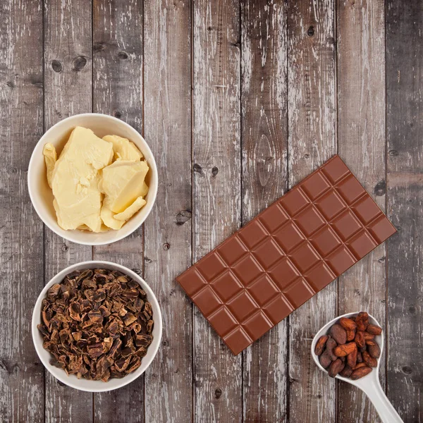 Bar of milk chocolate, cocoa butter, carob and cocoa beans on dark wooden background
