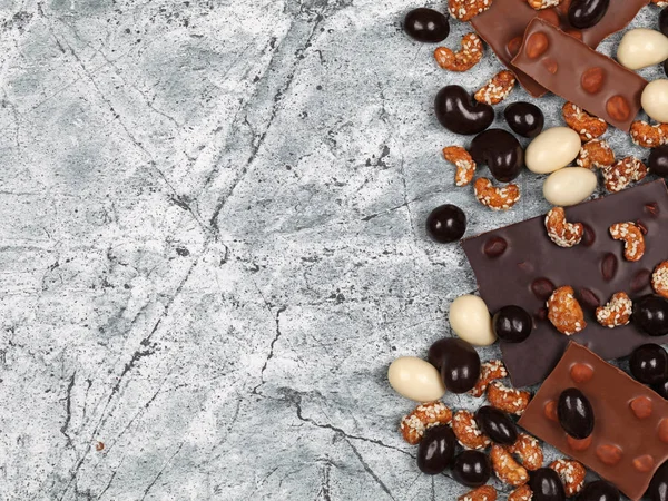 Mix of broken chocolate bars, sweet cashew and chocolate covered nuts on gray stone background