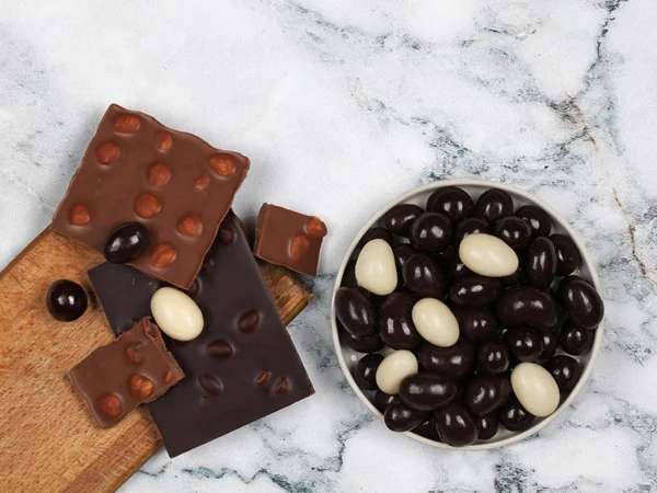 Broken chocolate bars and chocolate covered nuts on gray marble background