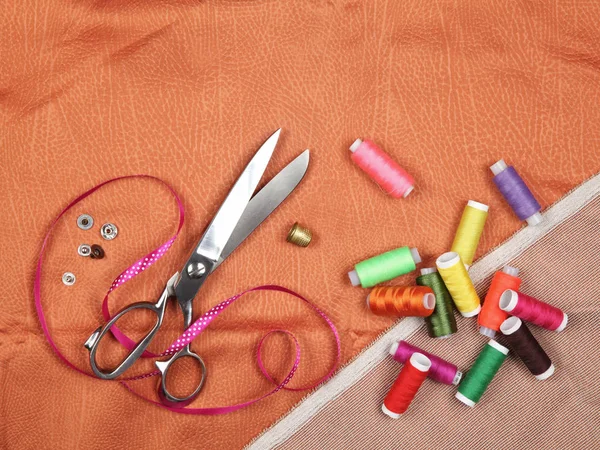 Set of tailoring tools and accessories on orange fabric. Top view, flat lay