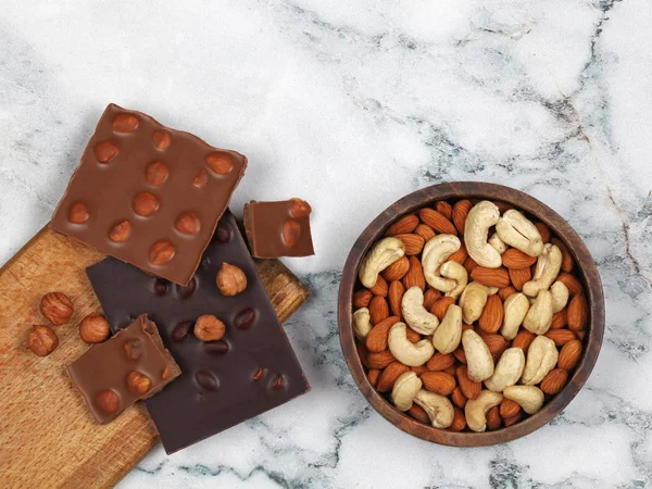 Zerbrochene Schokoriegel, rohe Haselnüsse, Mandeln und Cashew auf grauem Marmorhintergrund — Stockfoto