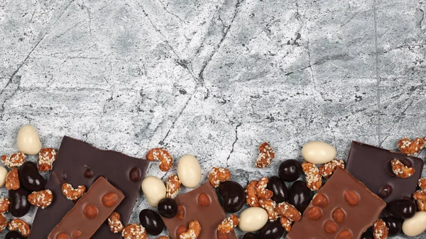 Mix of broken chocolate bars, sweet cashew and chocolate covered nuts on gray stone background