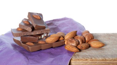 Kırık çikolatalı çikolata, badem ve bej leylak kağıtlı fındık. Yakın çekim.