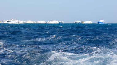 Mavi deniz suyunda yelken açan birkaç beyaz yat var.