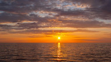 Gün batımı deniz manzarası. Suyun üzerindeki güneş bulutlu gökyüzünde 