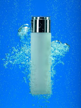 Mavi suda köpüklü beyaz gümüş bir şişe. Kozmetik ürünleri suyun altında yakın çekim