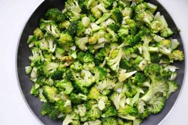 Beyaz zemin üzerinde bir tavada kavrulmuş ve kesilmiş taze sağlıklı brokoli lahana