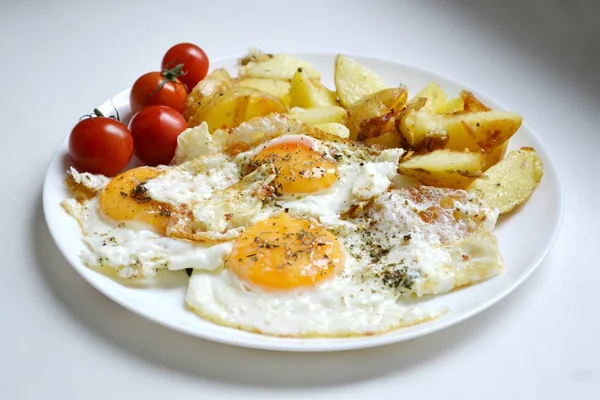 Grote ronde plaat vol met gebakken eieren, patat en cherry tomaten - een traditionele continentaal ontbijt — Stockfoto