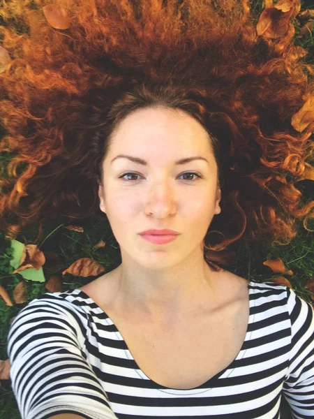Rüya gibi kızıl saçlı kadın ile sonbahar yaprakları yeşil çim üzerinde yalan — Stok fotoğraf