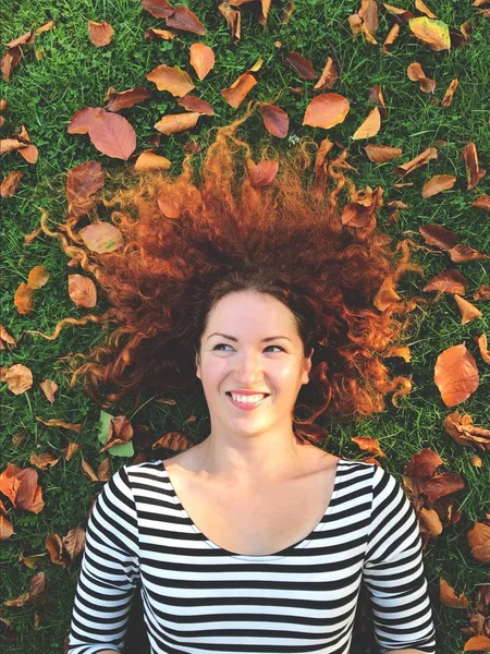 Dreamy redhead woman with autumn leaves lying on green grass — Stock Photo, Image