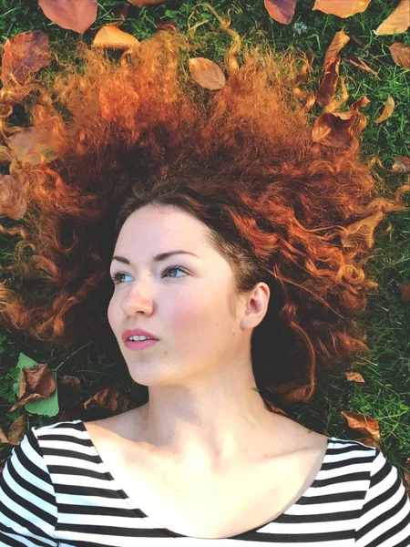 Dreamy redhead woman with autumn leaves lying on green grass — Stock Photo, Image