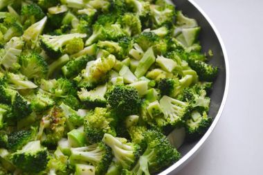 Beyaz zemin üzerinde bir tavada kavrulmuş ve kesilmiş taze sağlıklı brokoli lahana