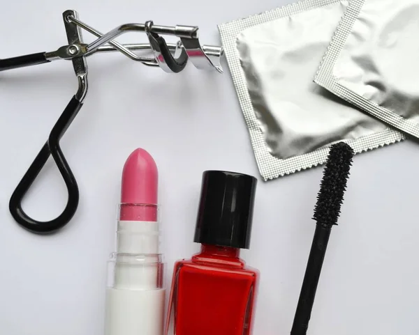 Paar van condooms en een cosmetica bezet met zwarte mascara, roze en rood nagellak en lippenstift en wimper krultang geïsoleerd op wit — Stockfoto