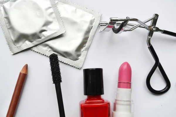 Paar van condooms en een cosmetica bezet met zwarte mascara, roze en rood nagellak en lippenstift en wimper krultang geïsoleerd op wit — Stockfoto