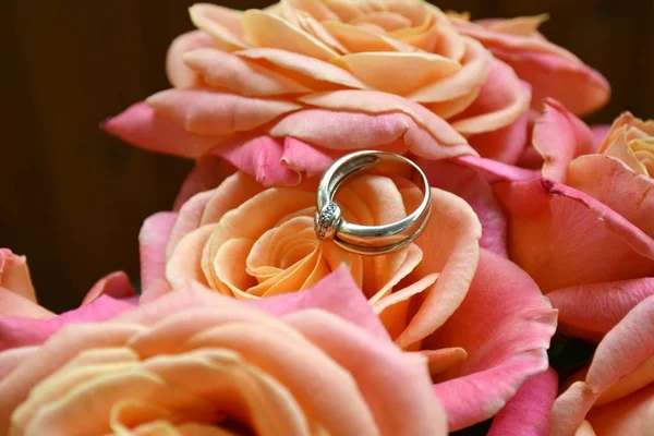在粉红色的玫瑰花的美丽婚礼花束上的两个金色的订婚戒指。 — 图库照片