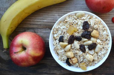 Çiğ yulaf gevreği ile fındık ve ahşap masa üzerinde beyaz kase kuru üzüm