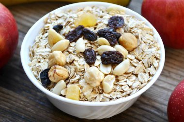 Çiğ yulaf gevreği ile fındık ve ahşap masa üzerinde beyaz kase kuru üzüm