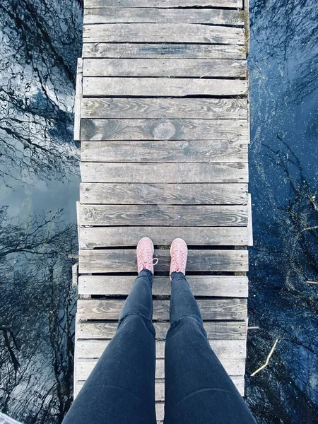 Outdoor walk by the river shown by jeans and sneakers wearing legs standing on an old wooden bridge