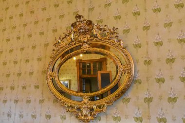 Cuenca, Ekvador; 10 Aralık 2019: Çiçekli duvar kağıdında asılı klasik altın ayna