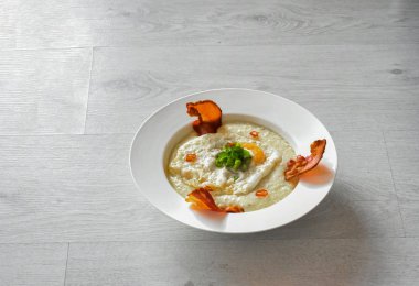 Side view of a plate of grits with fried egg, bacon and chives