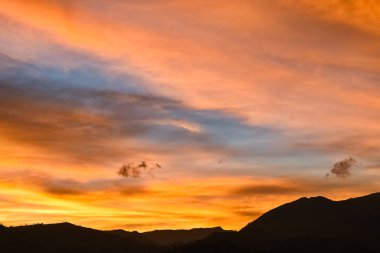 Bir dağın siluetinin üzerinde turuncu bulutlar olan çok renkli bir gökyüzü.