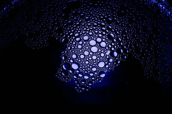 Blå oljedroppar från en blandning av vatten och olivolja upplyst med färgad glödlampa — Stockfoto