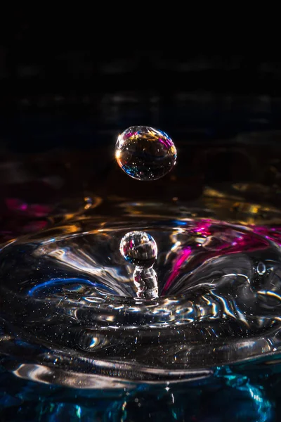 Water drops splash forming ripples and waves and abstract water columns in a colorful background — 스톡 사진