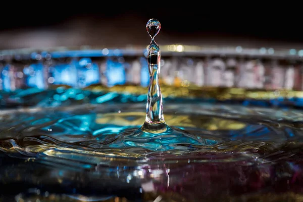 Water drops splash forming ripples and waves and abstract water columns in a colorful background — 스톡 사진