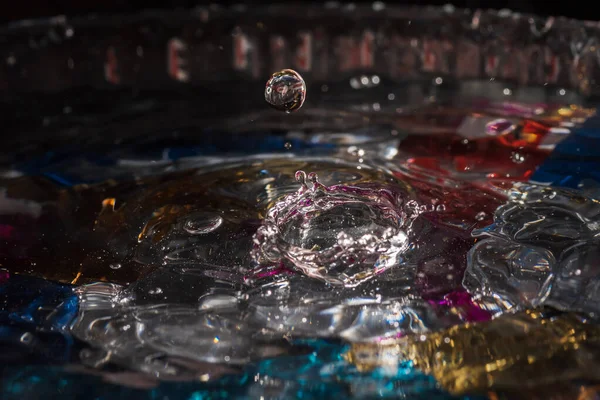 Water drops splash forming ripples and waves and abstract water columns in a colorful background — Stock Photo, Image