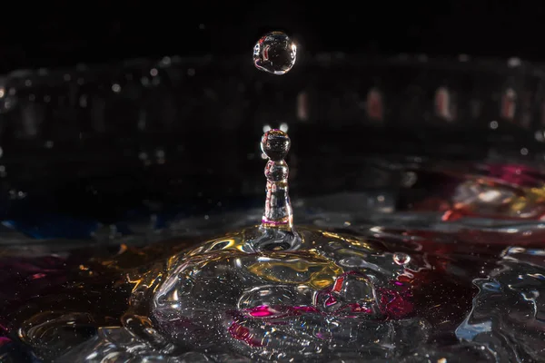 Water drops splash forming ripples and waves and abstract water columns in a colorful background — 스톡 사진