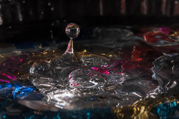 Water drops splash forming ripples and waves and abstract water columns in a colorful background — Stock Photo, Image