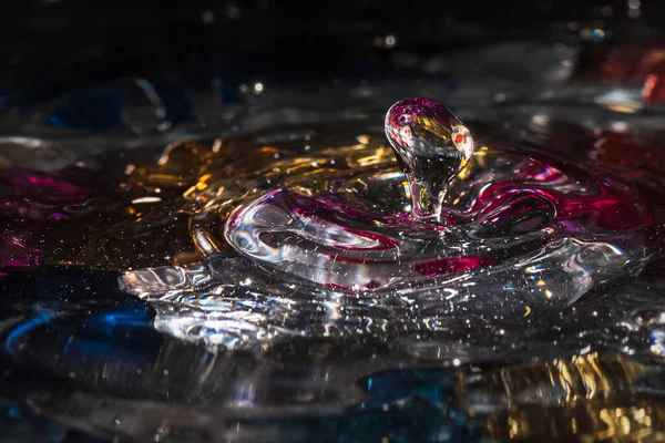 Water drops splash forming ripples and waves and abstract water columns in a colorful background — ストック写真