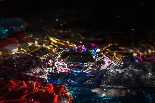 Water drops splash forming ripples and waves and abstract water columns in a colorful background — Stock Photo, Image