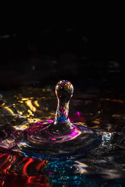 Water drops splash forming ripples and waves and abstract water columns in a colorful background — 스톡 사진