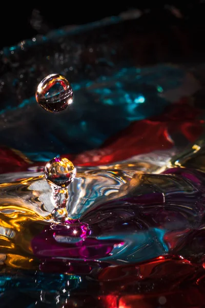 Water drops splash forming ripples and waves and abstract water columns in a colorful background — ストック写真