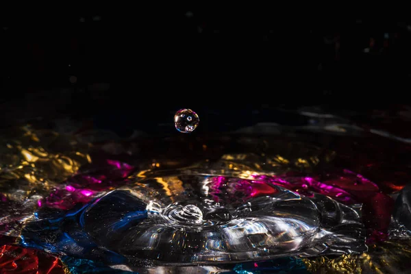 Water drops splash forming ripples and waves and abstract water columns in a colorful background — ストック写真