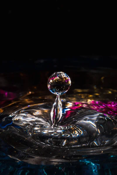 Water drops splash forming ripples and waves and abstract water columns in a colorful background — Stock Photo, Image