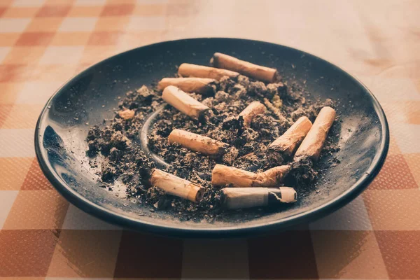 Sigara dolu kirli mavi kül tablası ve turuncu arka planda marihuana izmariti.