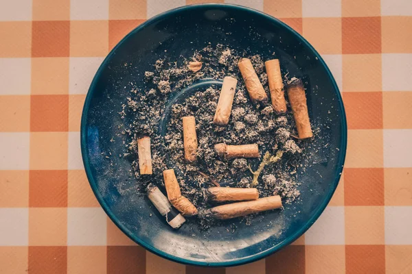 Sigara dolu kirli mavi kül tablası ve turuncu arka planda marihuana izmariti.