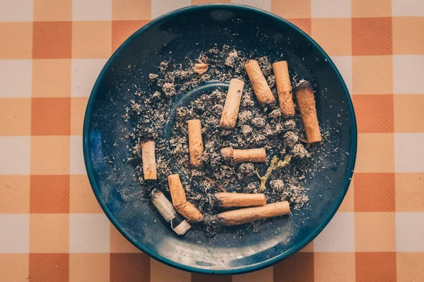 Sigara dolu kirli mavi kül tablası ve turuncu arka planda marihuana izmariti. Stok Fotoğraf