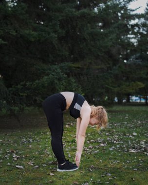 Mavi gözlü ve siyah elbiseli genç sarışın kız sıcak bir kış öğleden sonrasında parkta egzersiz yapıyor.