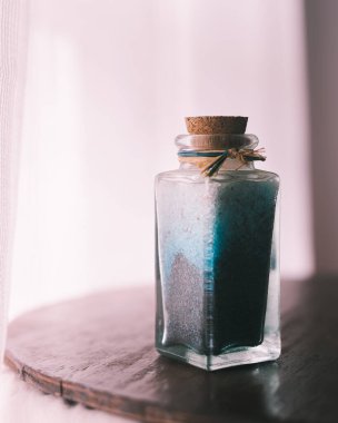 Doğal ışıkla aydınlatılmış beyaz arkaplanlı spa tedavilerini gevşetmek için mavi banyo tuzlarıyla süslü bir şişe.