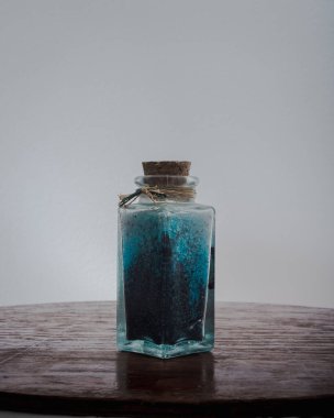 Doğal ışıkla aydınlatılmış beyaz arkaplanlı spa tedavilerini gevşetmek için mavi banyo tuzlarıyla süslü bir şişe.