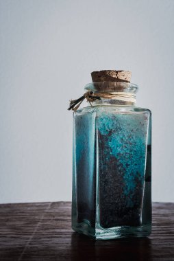 Doğal ışıkla aydınlatılmış beyaz arkaplanlı spa tedavilerini gevşetmek için mavi banyo tuzlarıyla süslü bir şişe.